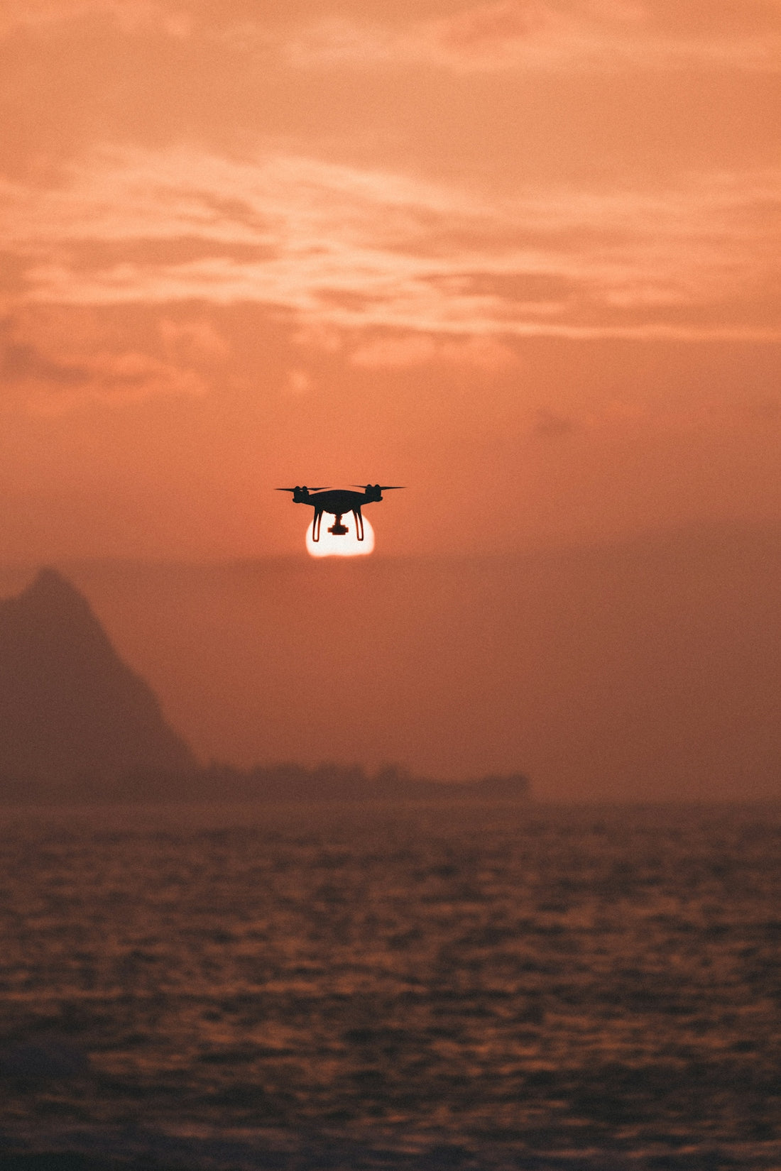 silhouette of drone hovering above body of water