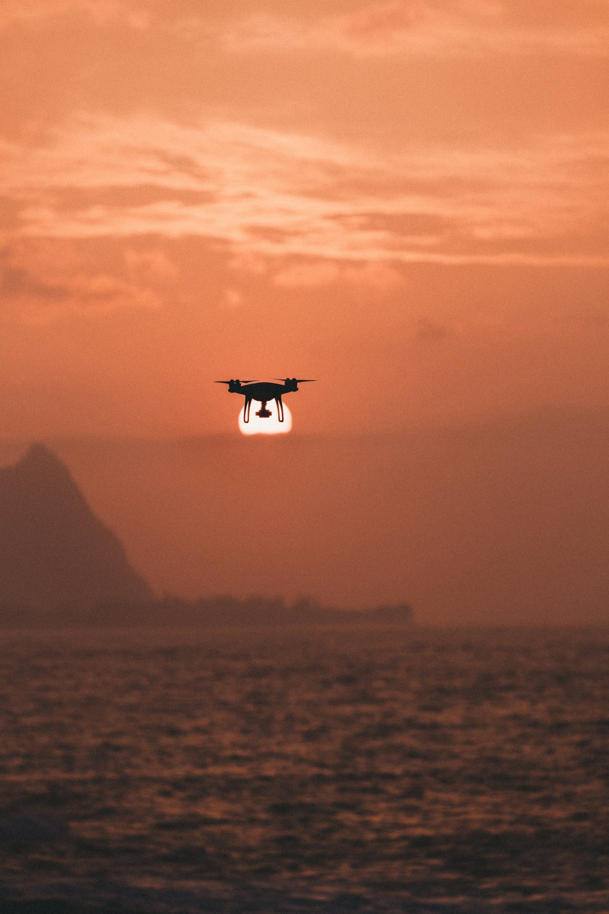 silhouette of drone hovering above body of water