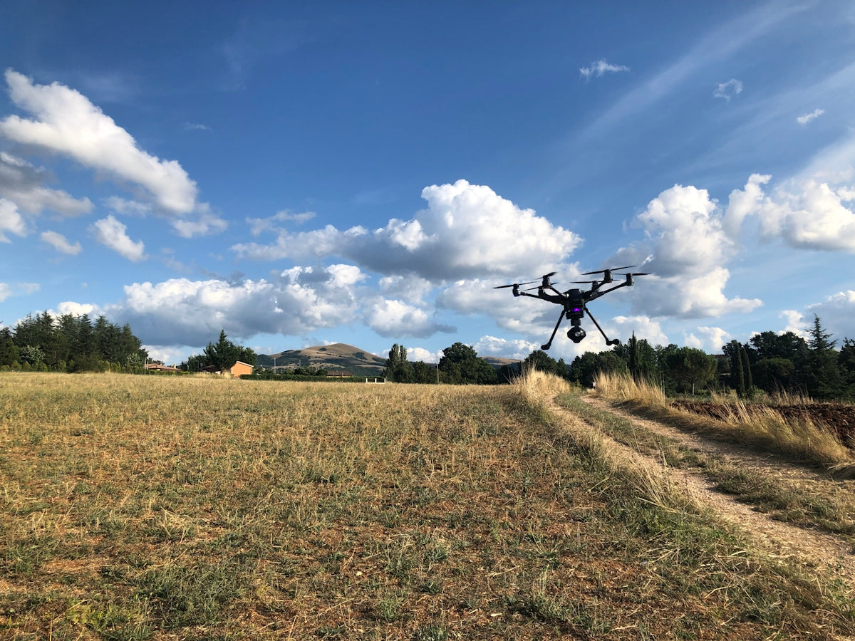 black drone near green field viewing mountain under blue and white skies during daytime