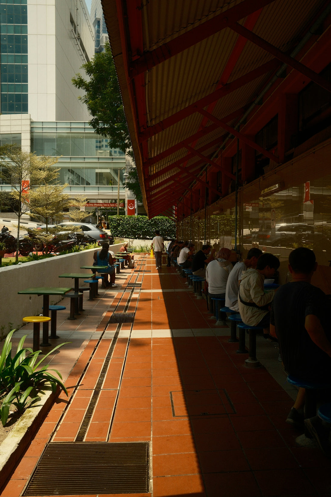 People sitting at tables along a shaded outdoor walkway.